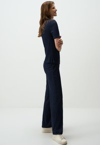 Marineblauw textuur tweedelig outfit bestaande uit een top met korte mouwen en brede broek, gecombineerd met witte sneakers. Soepele stof met een subtiel patroon.
