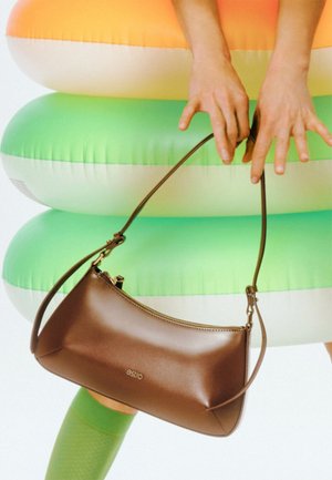 Braune Lederhandtasche mit geschwungenem Design, Reißverschluss und Schultergurt, vor bunten aufblasbaren Ringen platziert.