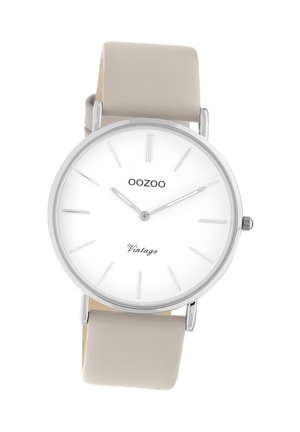 Montre argentée avec un cadran blanc, des repères horaires minimalistes et un bracelet en cuir beige clair. Le texte sur le cadran indique "OOZOO Vintage."