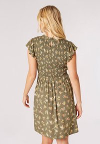 Olivengrünes Kleid mit Blumenmustern, gerafftem Mieder, Rüschensäumen und einem Schlüsselhole-Detail im Rücken. Leichter Stoff.
