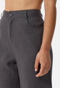 Grijze linnen broek heeft een soepele textuur, een voorzak en een enkele knoopsluiting in de taille. Op maat gemaakt voor een comfortabele pasvorm.