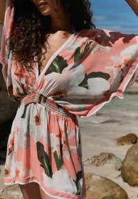 Rózsaszín és fehér virágmintás takaró. Átlátszó anyag, laza szabás, mély V-kivágás és ráncolt, elasztikus derék rész.