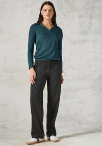 Tiefblaues Langarmoberteil mit Kragen und V-Ausschnitt, kombiniert mit dunkelgrauen, locker sitzenden Hosen und weißen Sneakers mit schwarzen Akzenten.