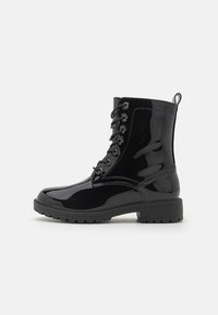 Botines de charol negro con cordones en la parte delantera, puntera redonda y suela de goma resistente. Presentan ojales metálicos y una cinta de tirón.