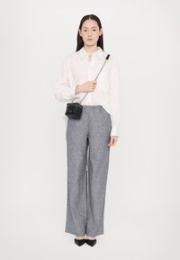 Bílá košile s dlouhými rukávy a knoflíky, šedé široké kalhoty, černá crossbody kabelka s řetízkovým popruhem a černé baleríny se špičatou špičkou.