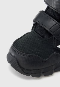 Must sportlik jalanõu tekstureeritud võrgu ja kummimaterjalidega, mis sisaldab pehmendatud keelega ja reguleeritavate takjapaeltega kindlalt kinnitumiseks.