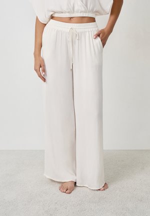 Pantalones de pierna ancha en un beige claro, fabricados con un tejido suave, que cuentan con una cinturilla elástica con cordón y bolsillos laterales.