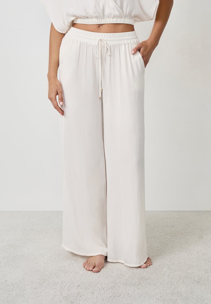 Pantalones de pierna ancha en un beige claro, fabricados con un tejido suave, que cuentan con una cinturilla elástica con cordón y bolsillos laterales.