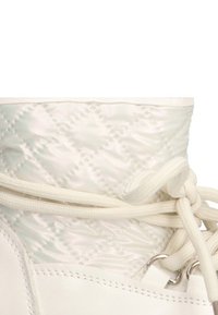 Bota de tobillo blanca con un upper acolchado brillante y una parte inferior de cuero suave. Equipadas con cordones blancos y ojales metálicos.