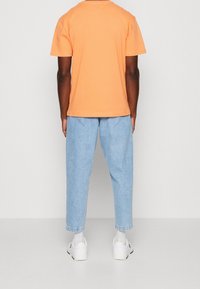 Oranžové bavlněné tričko s uvolněným střihem, spárované se světle modrými džíny. Bílá sportovní obuv dotváří celý outfit.