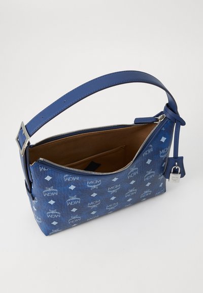 Sac à épaule en cuir bleu avec motif logoté MCM en relief, matériel en argent, fermeture zippée et poche intérieure marron. Bandoulière ajustable incluse.