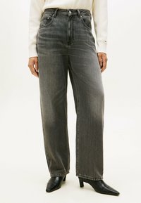 Hoge taille, wijde jeans in vervaagd zwart denim. Heeft een klassiek vijf-pocket ontwerp en contrasterende stiksels. gedragen met puntige hakken.