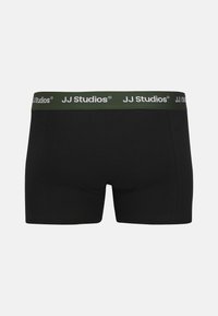 Schwarze Boxerbriefs aus weichem Material mit grünem elastischem Bund, der das weiße Logo "JJ Studios" trägt. Einfaches, figurbetontes Design.