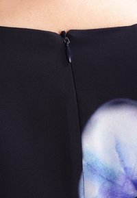 Robe en tissu noir au toucher lisse, dotée d'une fermeture éclair discrète dans le dos et présentant un motif floral coloré sur un côté.