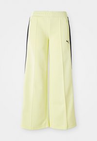 Light yellow sweatpants with black side stripes, elastic waistband, and zipper pockets. Features a Puma logo on the left side.