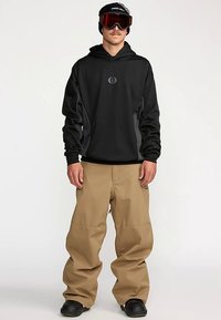 Black hooded sweatshirt with gray accents, paired with loose-fitting tan pants and black boots. User wears sunglasses and a black cap.