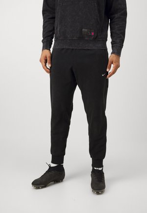 Zwarte Nike-sweater met een voorzak en label; gecombineerd met bijpassende zwarte joggingsbroek en zwarte voetbalschoenen met noppen.