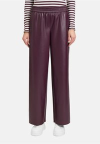 Bordeaux neplederen broek met wijde pijpen, een elastische tailleband, een gladde textuur en gecombineerd met witte sneakers.
