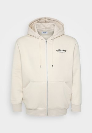 Kreemvärvi tõmbluku ja nööridega kapuutsiga sviiter, ees on taskud, varrukate ääred on soonilised ning rinnal on must "JJ Studios" logo. Pehme kangastekstuuri.