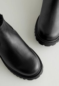 Czarne skórzane botki za kostkę z textured powierzchnią, okrągłym noskiem i grubą gumową podeszwą z ząbkowanym brzegiem. Dwa boczne otwory ułatwiające zakładanie.