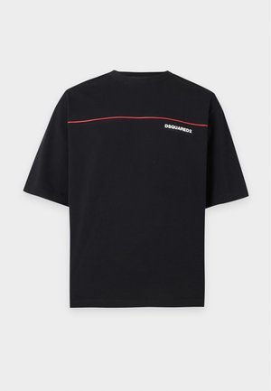 Giovane uomo in piedi che indossa una maglietta nera con una linea rossa e testo bianco, jeans blu e scarpe da ginnastica nere su uno sfondo bianco uniforme.