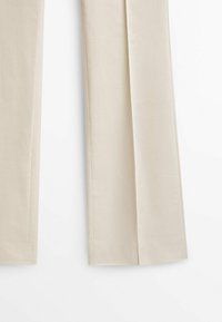 Pantalon beige sur mesure avec une texture lisse, jambes droites et un pli discret à l'avant. Design minimaliste, sans aucune pièce métallique apparente.