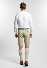 Lysgrønne shorts med en tætsiddende pasform, beige knæstrømper og brune sko. Den hvide skjorte har en button-down krave.