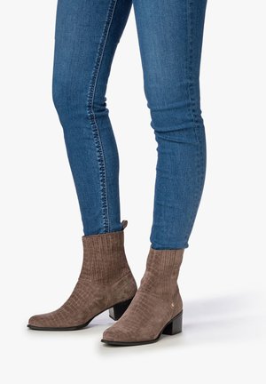 Braune, krokodilpräge Stiefeletten mit geripptem Schaft und Blockabsatz, kombiniert mit blauen Skinny Jeans. Strukturierte Wildleder-Oberfläche.