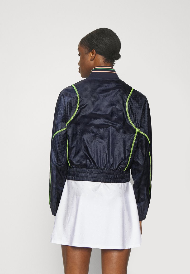 Veste bomber en bleu nuit, avec une finition brillante, rehaussée d'accents vert fluo, col côtelé et taille élastique, présentant un design de tissu texturé.