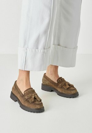 Braune Wildleder-Tassel-Loafer mit dicken schwarzen Sohlen, getragen zu weißen, weit geschnittenen, kurz geschnittenen Hosen.