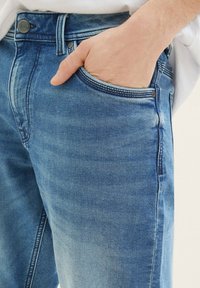 Jeans de mezclilla azul claro con un diseño clásico de cinco bolsillos, con un bolsillo para monedas visible y detalles de costura en contraste.