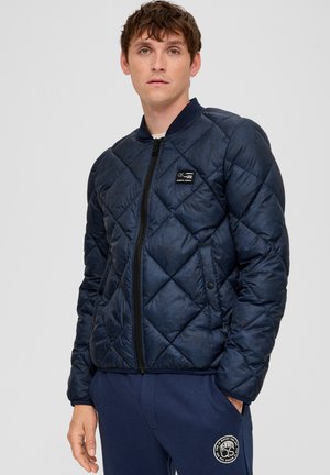 Marineblauwe gewatteerde bomberjack met een rits aan de voorkant, ribgebreide kraag en logo-patch. Beschikt over een zachte textuur en een warme, gevoerde uitstraling.