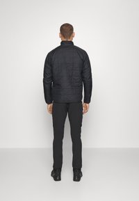 Czarna pikowana kurtka z stojącym kołnierzem, z długimi rękawami i teksturowanym wykończeniem, w połączeniu z czarnymi spodniami i solidnym obuwiem.