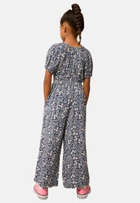 Blå blommig jumpsuit med korta ärmar, elastisk midja, vida ben och blommönster; matchad med rosa sneakers.