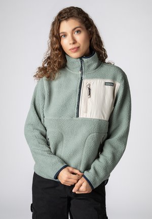 Fleece-Pullover in Pastellgrün mit hohem Kragen, seitlichen Taschen und einem cremefarbenen Taschenpanel. Verfügt über einen Reißverschluss und marineblaue Akzente.