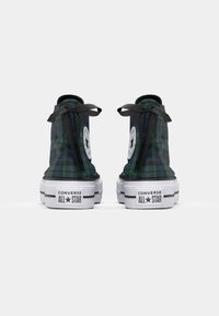 Wysokie trampki Converse w kratę w kolorze niebieskim i zielonym z czarnymi sznurowadłami, z białym logo gwiazdy i białą podeszwą z czarnymi akcentami.