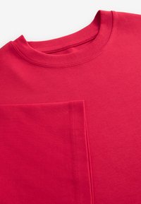 Rød bomuld T-shirt med ribbet rund hals. Har en stor lomme foran med kontrastsyning. Glat tekstur, enkelt design.