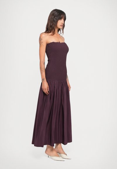 Bordeaux strapless maxi-jurk met een gerimpelde lijfje en geplooide rok, gemaakt van een gladde stof. Heeft een ruches halslijn en een A-lijn vorm.
