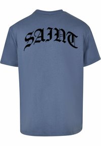 Mørkeblå bomullst-skjorte med store svarte bokstaver "SAINT" i stilisert skrift på baksiden. Korte ermer, normal passform og glatt tekstur.