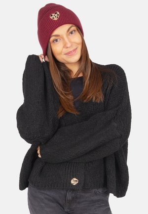 Black knitted sweater with oversized sleeves and ribbed hem, paired with a maroon beanie featuring a leopard print heart patch.