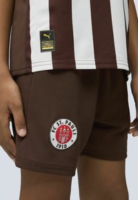Bruna fotbollsshorts med en vit FC St. Pauli-logotyp, prydda med en randig brun och vit tröja med en svart Puma-tagg.