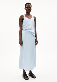 Lichtblauwe, mouwloze jurk met een relaxte pasvorm, gedrapeerd stof en maxi-lengte. Gecombineerd met zwarte loafers voor contrast.