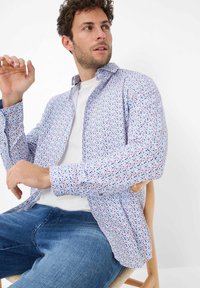 Langærmet skjorte med en lys blå baggrund og farverigt prikmønster, knap-ned krave og blødt stof. Bæres over en hvid t-shirt.