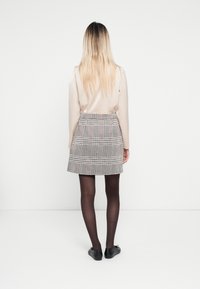 Beige langærmet top, grå rutet nederdel med plisseringer, sorte strømpebukser, og sorte flade sko. Fokus på rene linjer og struktureret silhuet.