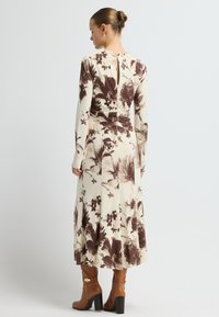 Sukienka z długim rękawem w kremowym kolorze z brązowym kwiatowym nadrukiem; dopasowana talia, rozszerzany dół i małe otwarcie z tyłu. Brązowe botki na obcasie dopełniają całość.