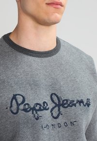 Grauer Pullover mit rundem Ausschnitt, mit einem dunkelblauen Schriftzug "Pepe Jeans London". Weicher, strukturierter Stoff.