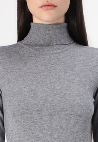 Gray turtleneck sweater made of a soft, knitted material. Features a fitted design and ribbed collar with a smooth texture.