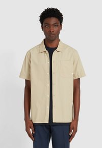 Korte mouwen, lichtbeige shirt met een knoopsluiting aan de voorkant, één borstzak en een relaxte pasvorm. De stof lijkt soepel en lichtgewicht te zijn.