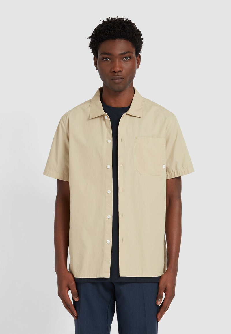 Korte mouwen, lichtbeige shirt met een knoopsluiting aan de voorkant, één borstzak en een relaxte pasvorm. De stof lijkt soepel en lichtgewicht te zijn.