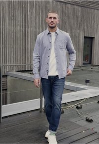 Ljusblå skjorta med vita prickar, kombinerad med en vit t-shirt och mörkblå jeans, komplett med vita sneakers.